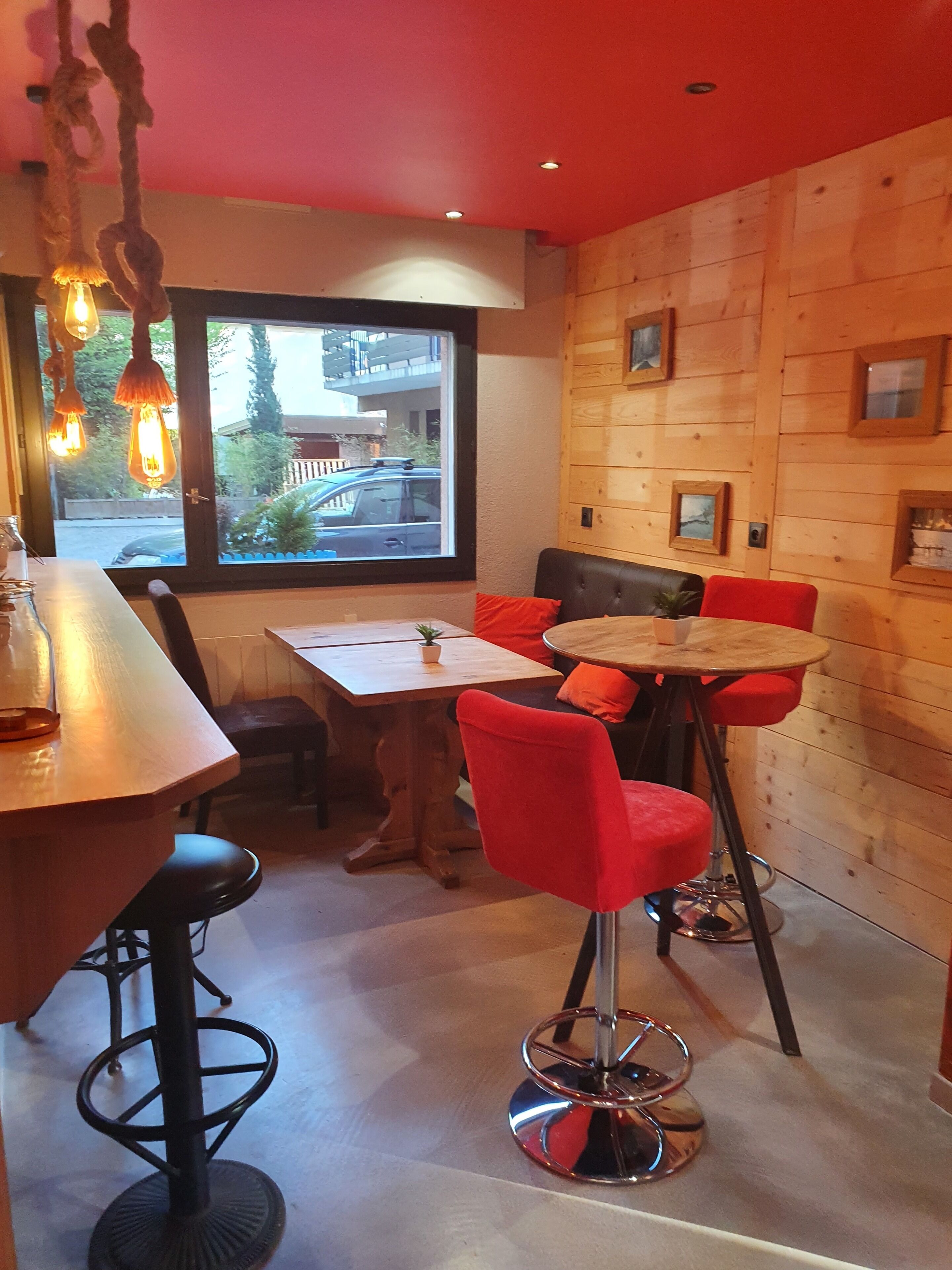 L’intérieur d’un restaurant avec un mur en bois, une grande fenêtre et un mélange de chaises rouges et noires.