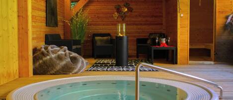 A wooden cabin interior with a hot tub, seating area, and a fireplace.
