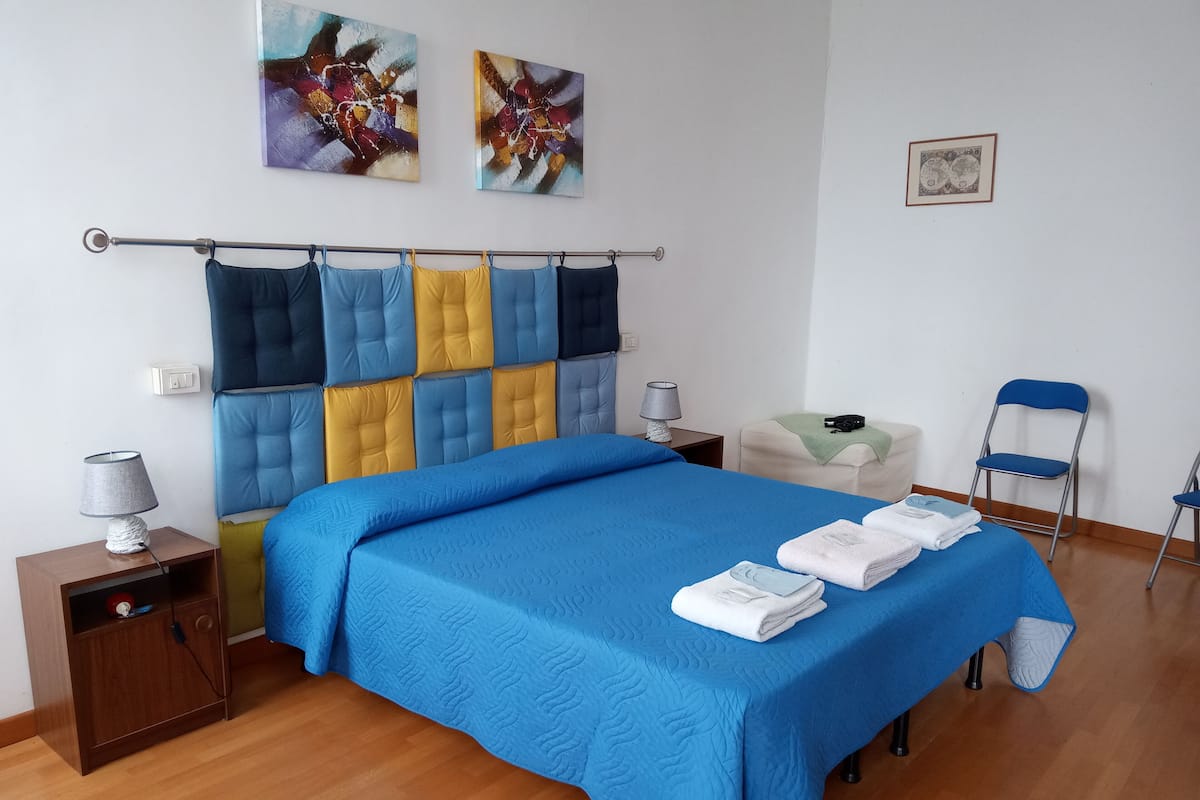 A neatly arranged bedroom with a bed, bedside tables, a chair, and artwork on the wall.