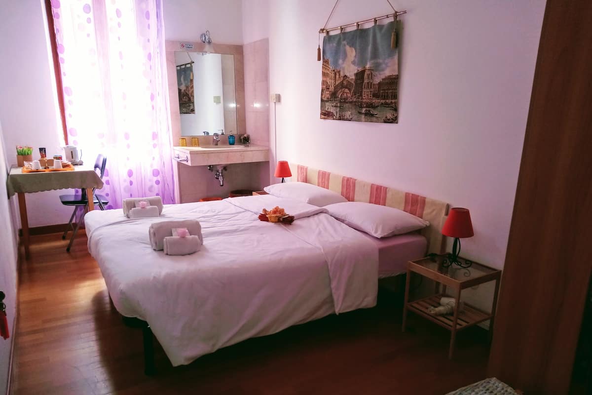A hotel room with a bed, bedside table, lamp, and a painting of a cityscape.