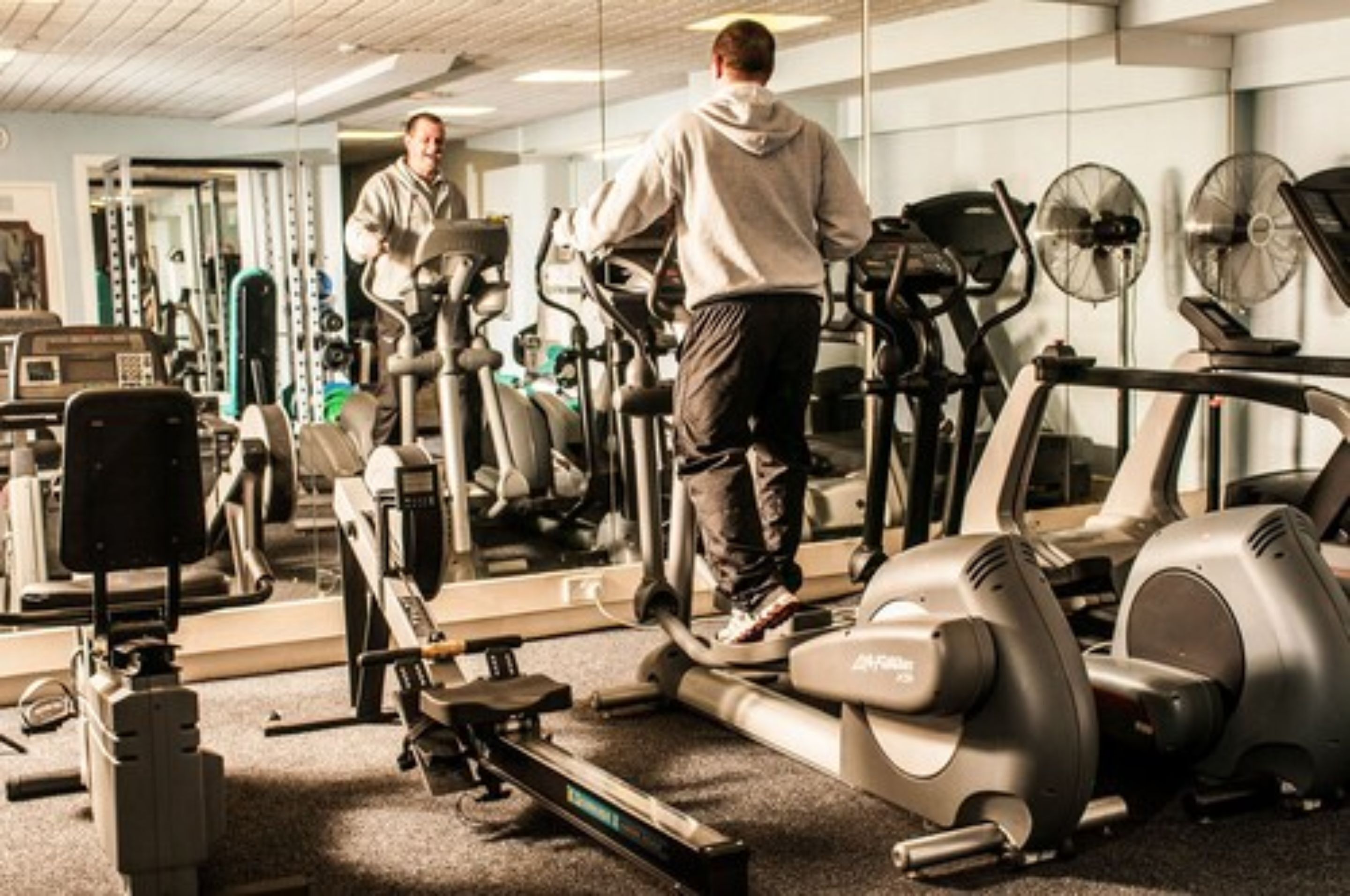 Un gimnasio con equipo de ejercicio, un espejo grande y una persona usando una cinta de correr.