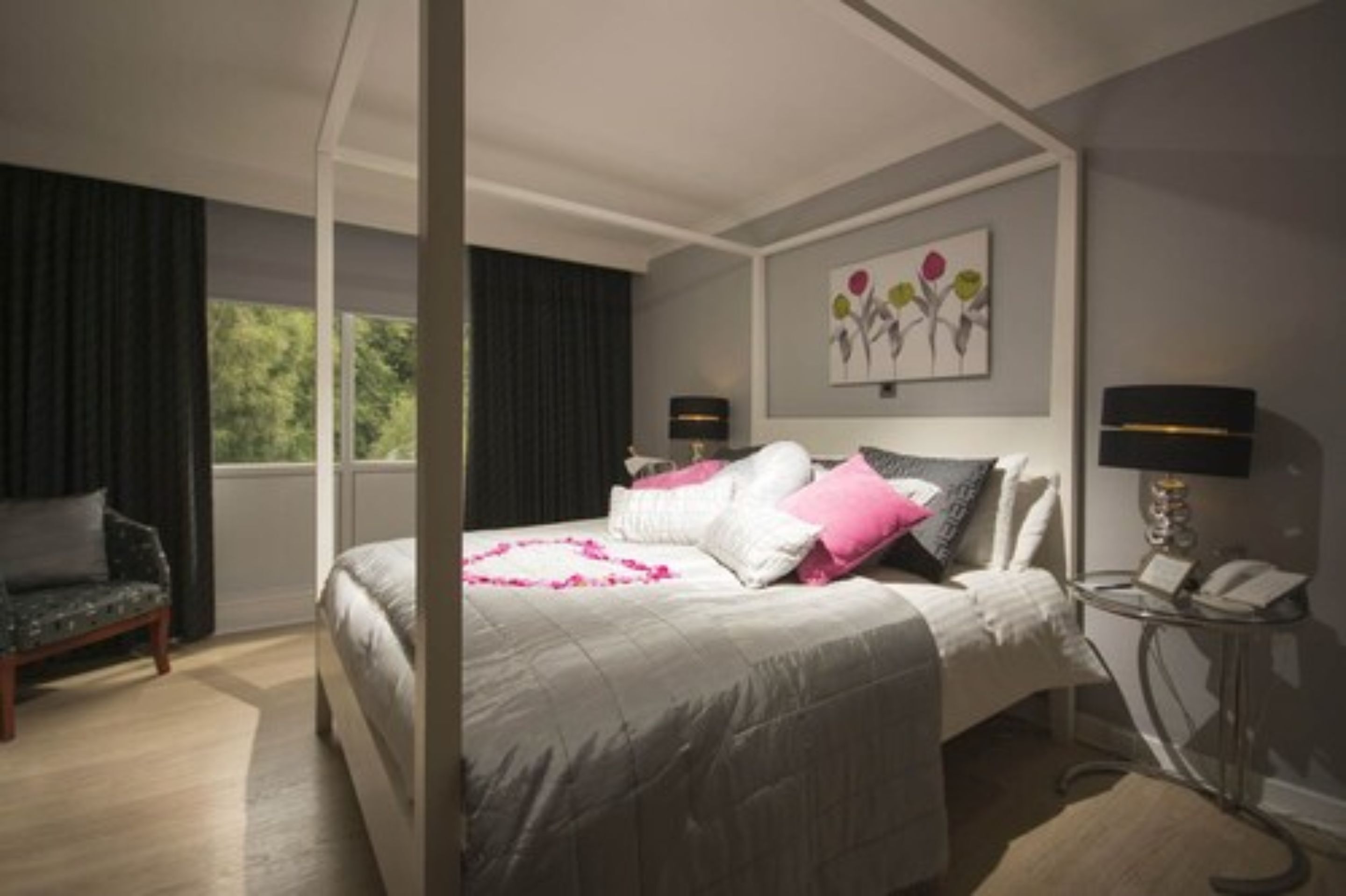 Un dormitorio moderno con una cama grande, una mesita de noche con lámpara, una silla y una ventana con cortinas.