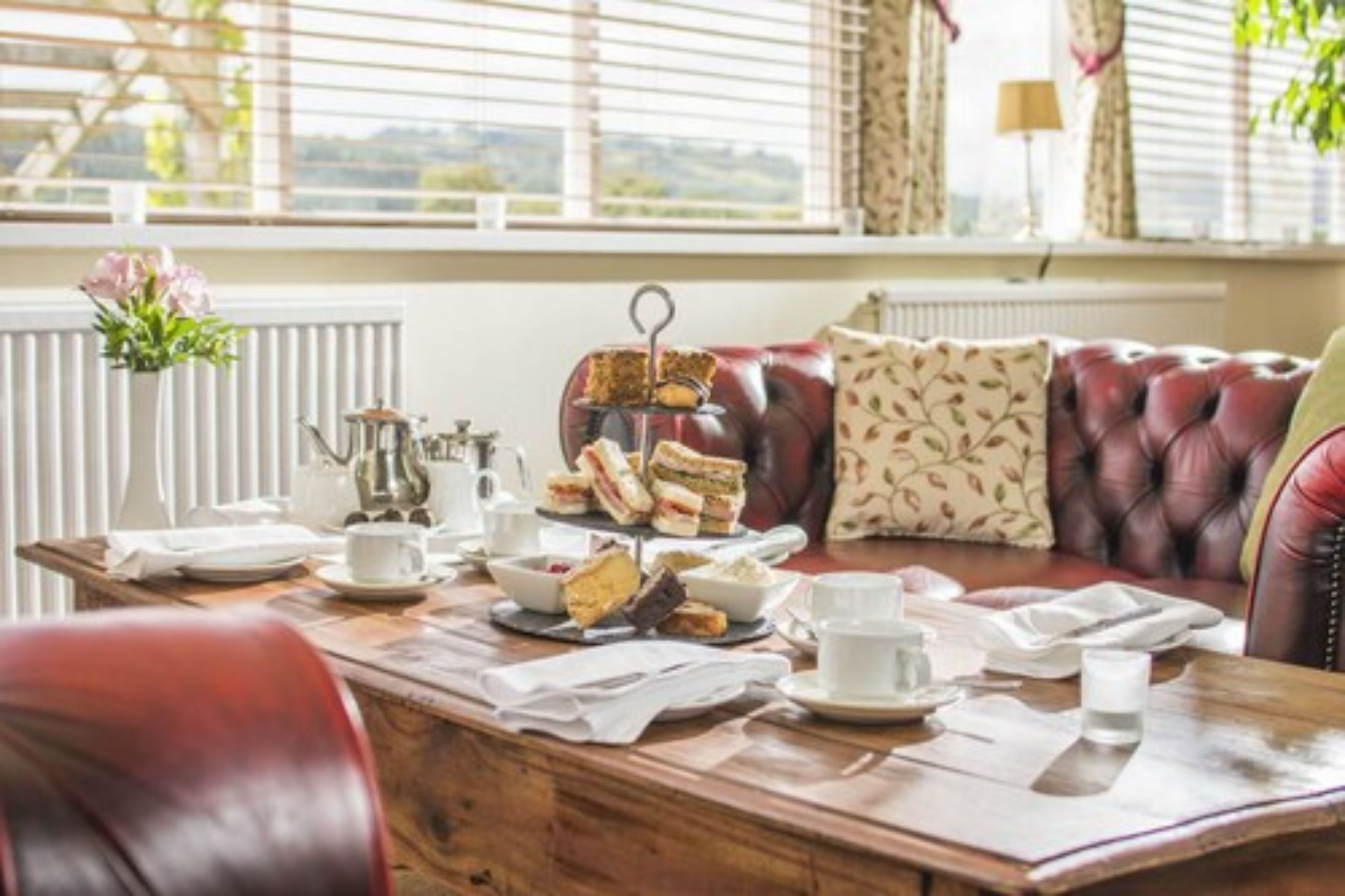 A dining table set with sandwiches, a teapot, cups, and saucers.