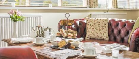 A dining table set with sandwiches, a teapot, cups, and saucers.