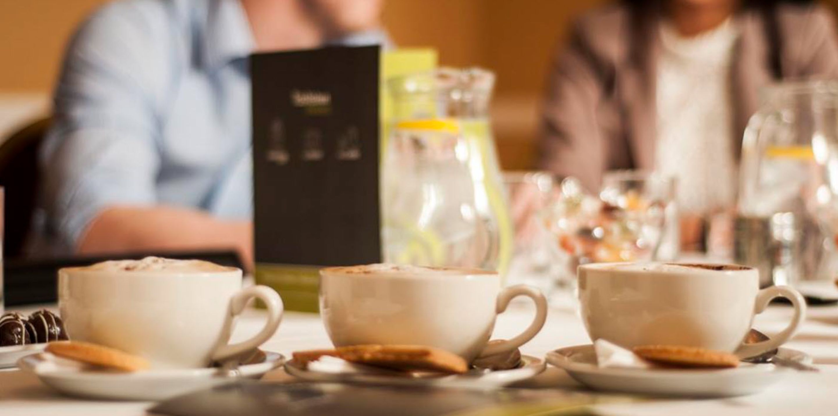 Una mesa con tres tazas de chocolate caliente, un menú y una jarra de vidrio.