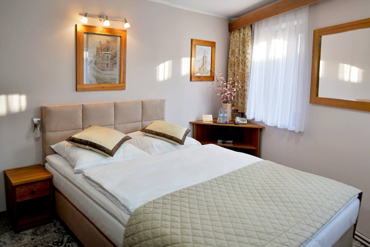 A hotel room with a large bed, two bedside tables, a nightstand, a small cabinet, and a mirror on the wall.