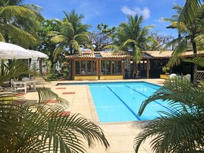 Une piscine dotée d’une terrasse carrelée, entourée de palmiers et agrémentée d’un espace salon abrité.