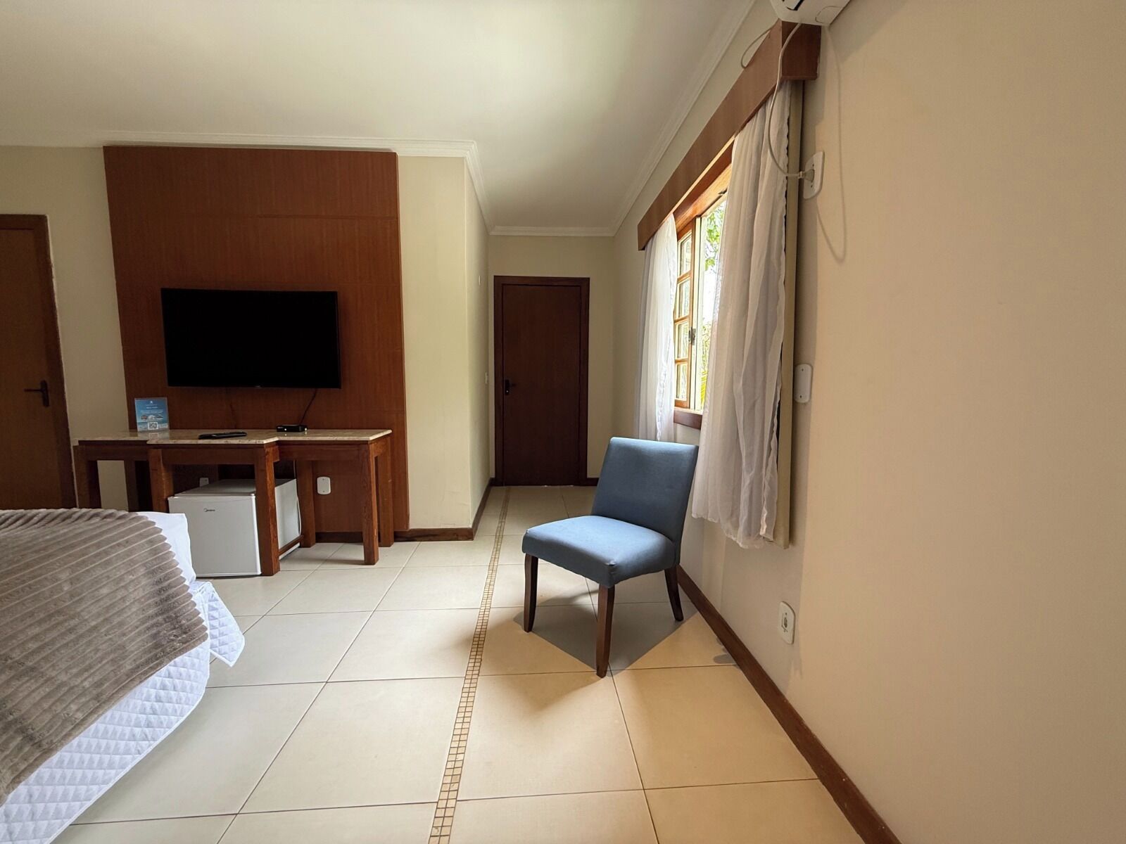 A hotel room with a bed, a desk with a television, a chair, and a window with curtains.