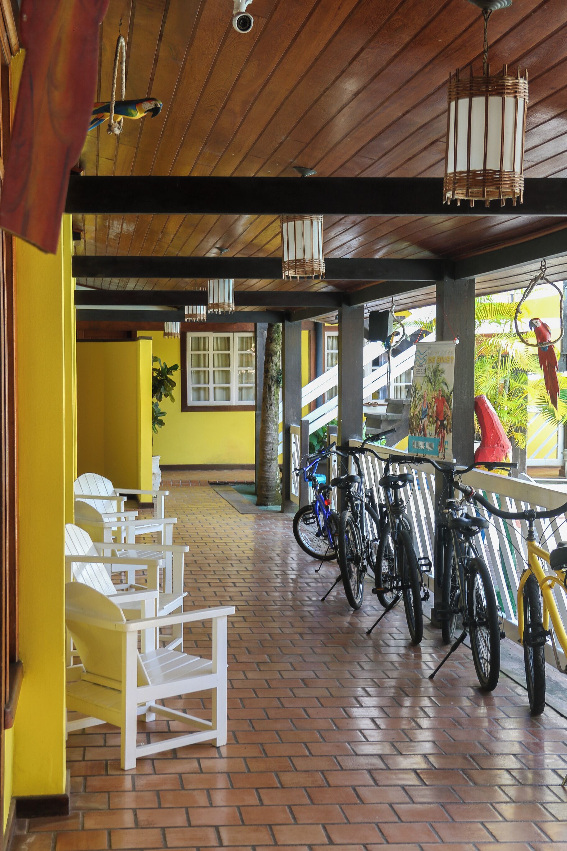 A covered outdoor seating area with white chairs, bicycles, and a wooden ceiling.