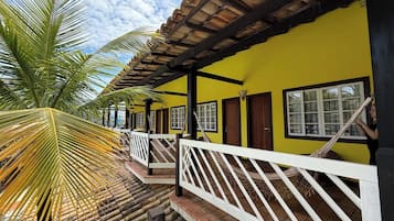 Un edificio amarillo con techo de tejas, barandillas blancas y una palmera.