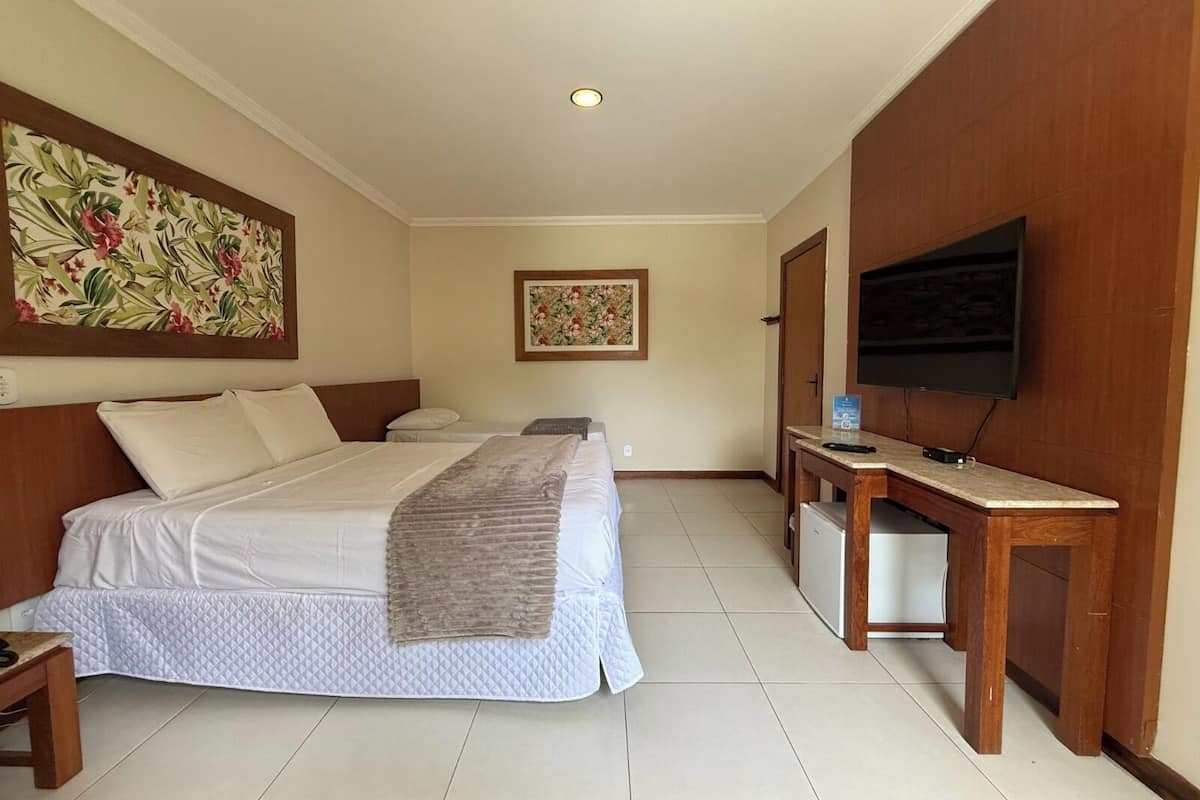 Une chambre d’hôtel avec un grand lit, un bureau avec une télévision et deux petits lits.