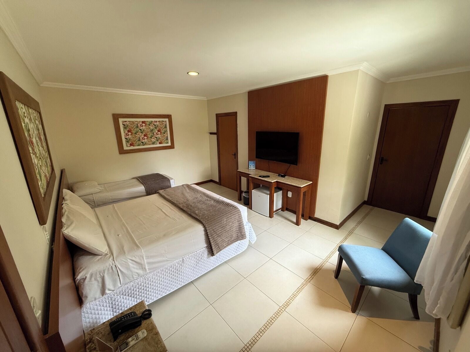 A hotel room with two beds, a desk with a TV, a chair, and a door.