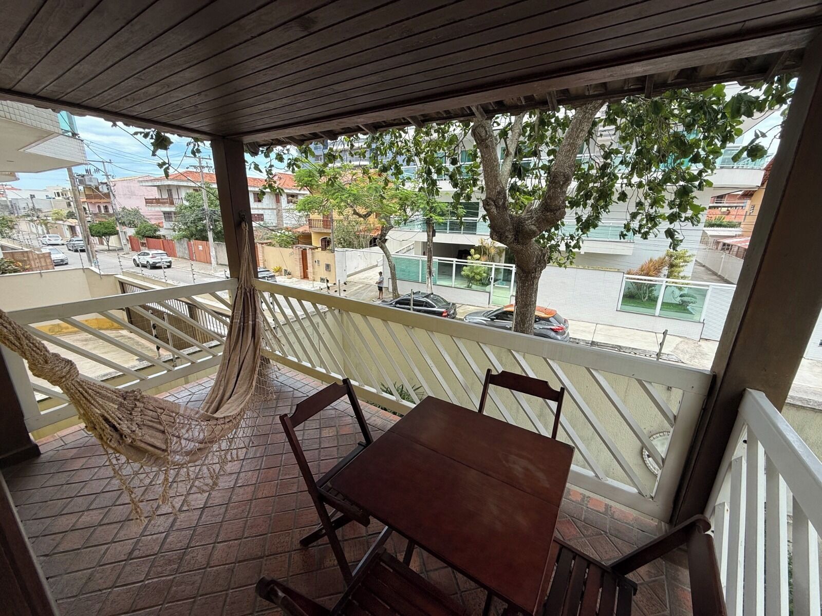 A balcony with a hammock, wooden table, and chairs.