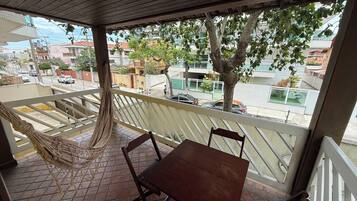 A balcony with a hammock, wooden table, and chairs.