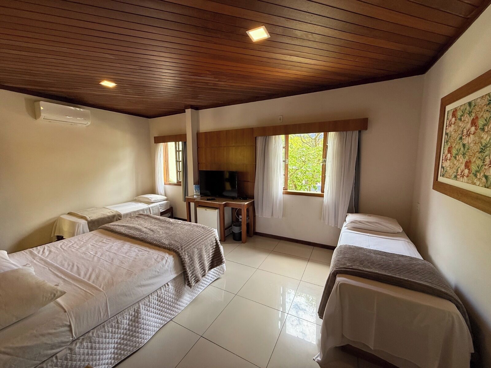 A hotel room with two beds, a desk, a television, and a window with curtains.