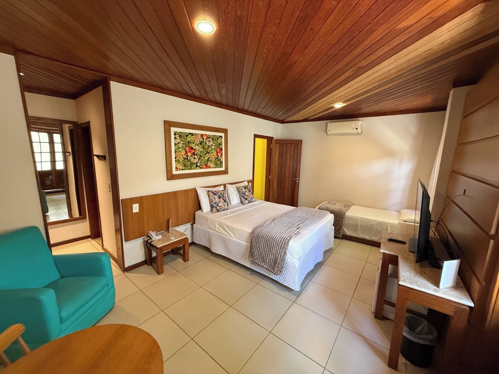 A bedroom with a bed, a desk, a chair, a television, and a painting on the wall.
