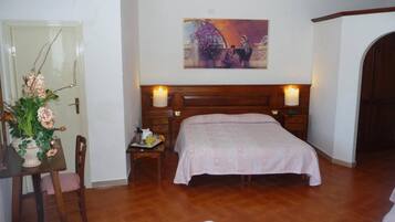 Una camera da letto con un letto di legno, un comodino, una sedia, un tavolo con un vaso di fiori e un quadro appeso al muro.
