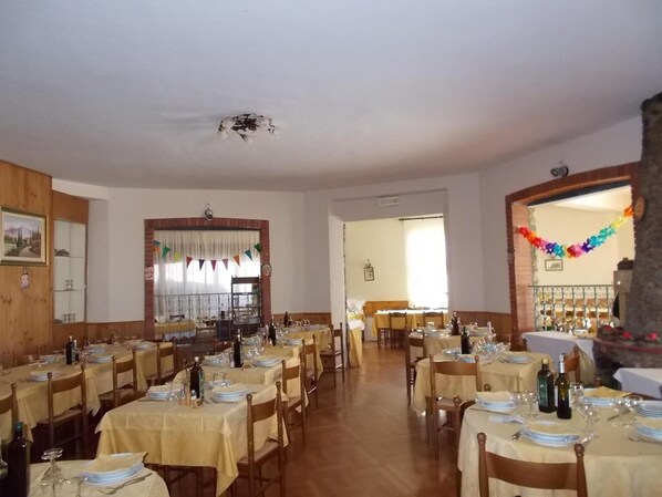 Un comedor con varias mesas dispuestas para comer, paredes de madera y vista a otra habitación.