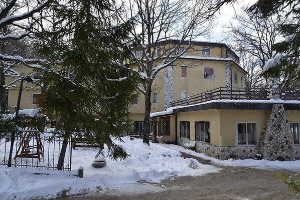 A multi-story building with a yellow facade, a stone staircase, and a snow-covered ground. - Albergo del Sole (Roccaraso)