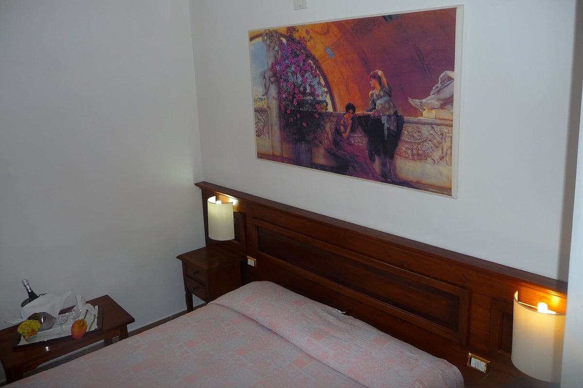 A hotel room with a bed, a nightstand, a lamp, and a painting on the wall.