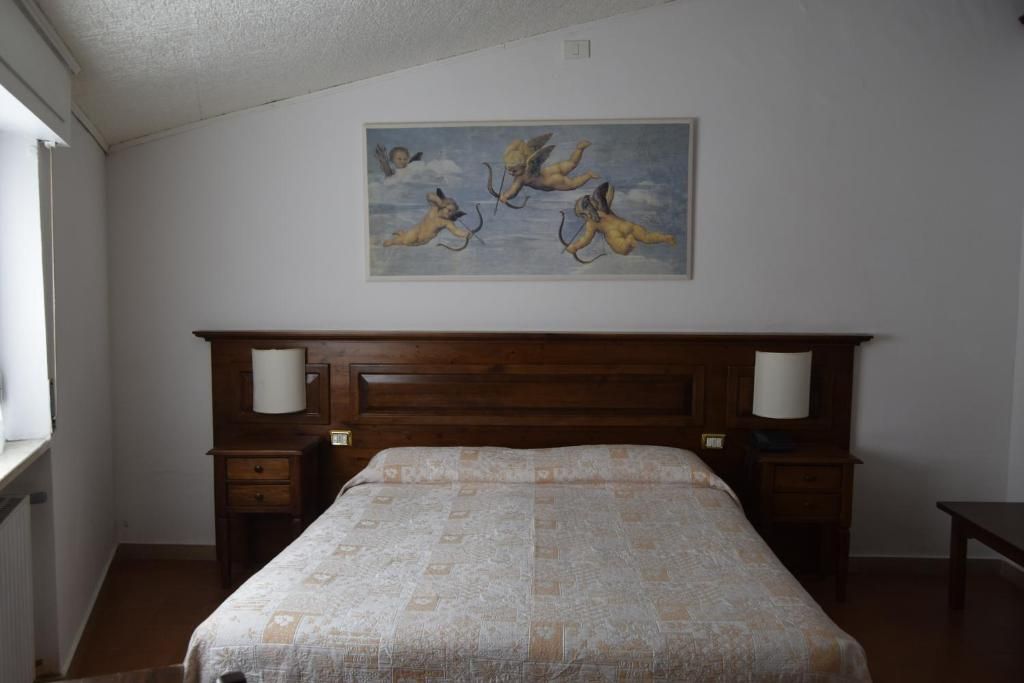 A bedroom with a wooden headboard, a bed with a patterned bedspread, two bedside tables with lamps, and a painting of cherubs on the wall.