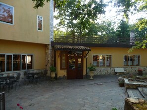 Un patio al aire libre con suelo de piedra, una puerta de madera y una zona de estar con mesas y sillas.