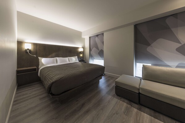 Une chambre moderne avec un grand lit, une table de chevet, une commode, un canapé et une grande fenêtre donnant sur un beau paysage.
