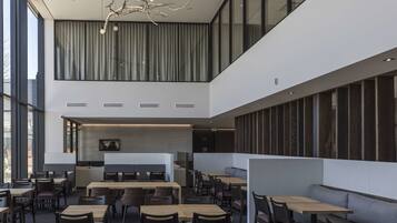 A modern restaurant with high ceilings, large windows, and a mix of seating options including tables and booths.