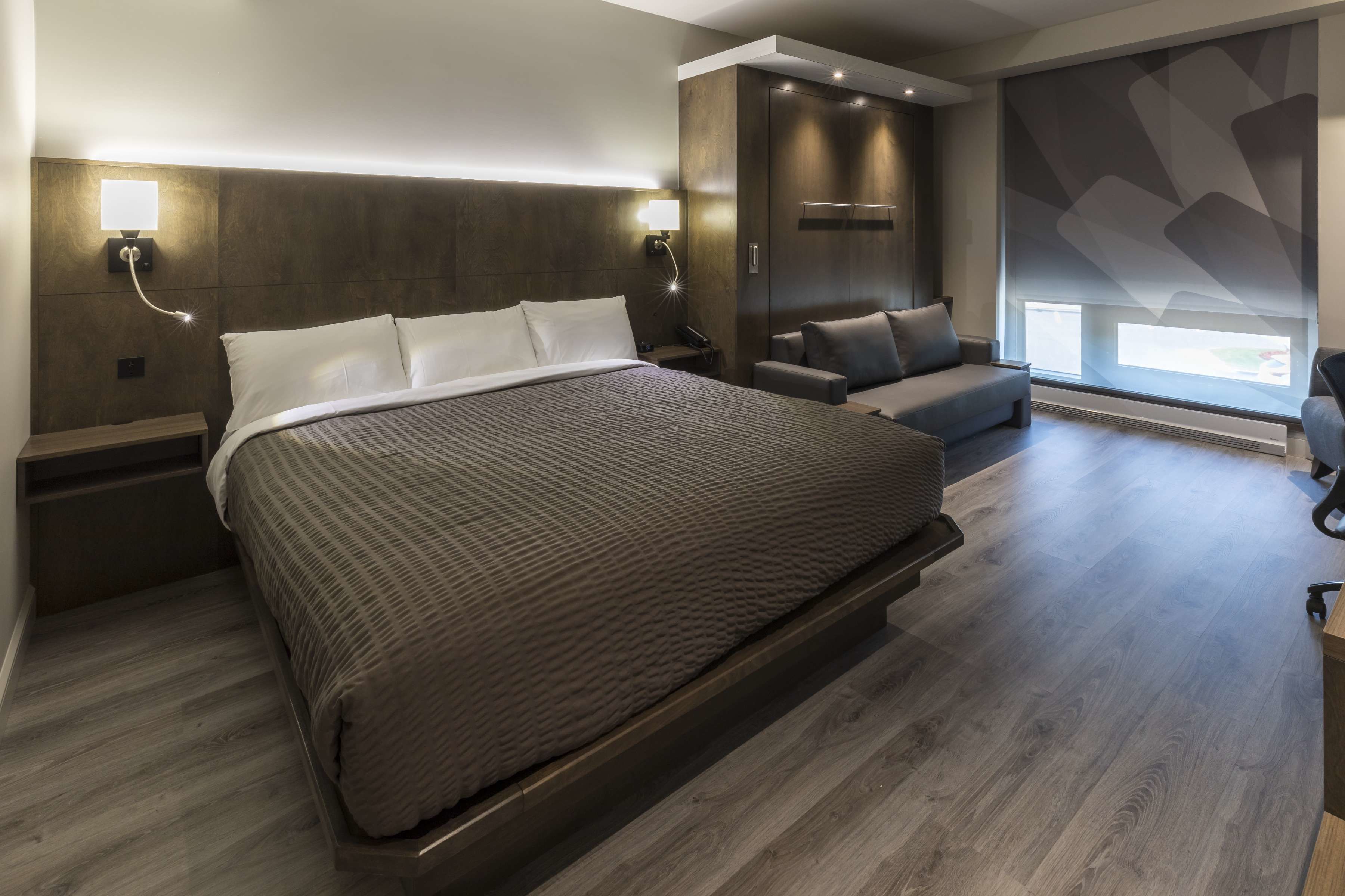 A modern hotel room with a large bed, a sofa, and a desk.