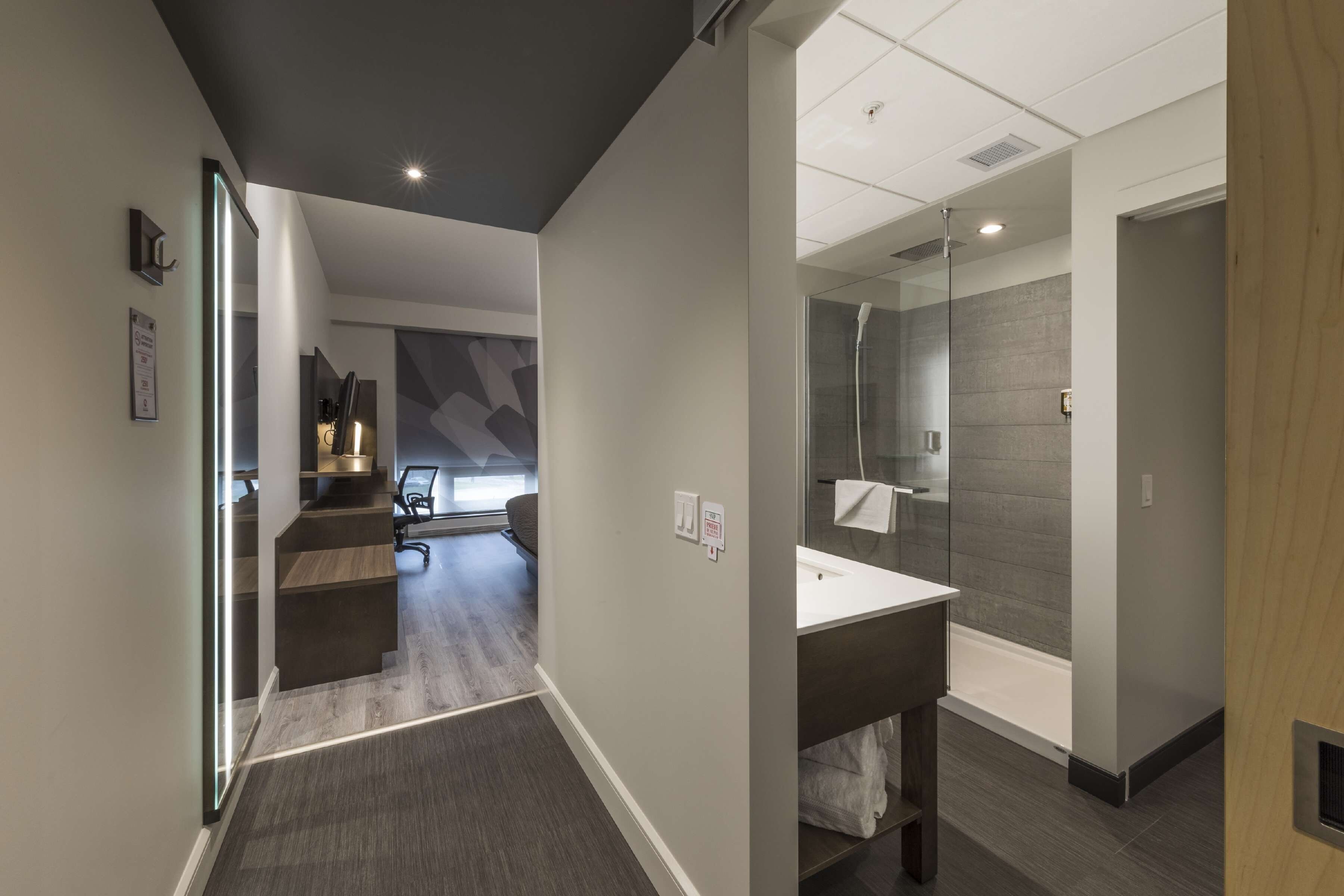 Un pasillo moderno de hotel con una escalera que lleva a una sala de conferencias, un baño con ducha de vidrio y un mostrador de recepción.