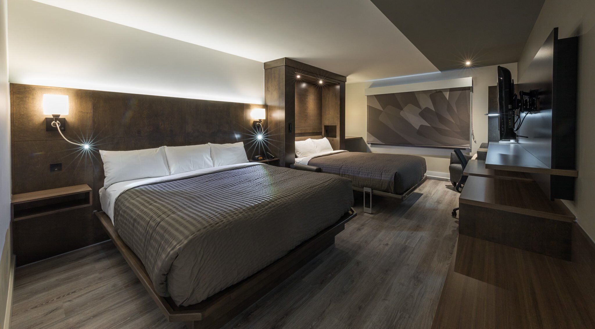 A modern hotel room with two beds, a desk, and a large flat-screen TV.
