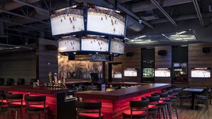 Un bar sportif doté de plusieurs écrans diffusant des matchs de hockey, un espace bar avec des tabourets et un intérieur en bois.