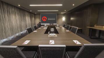 A conference room with a long table, chairs, a podium, and a logo on the wall.