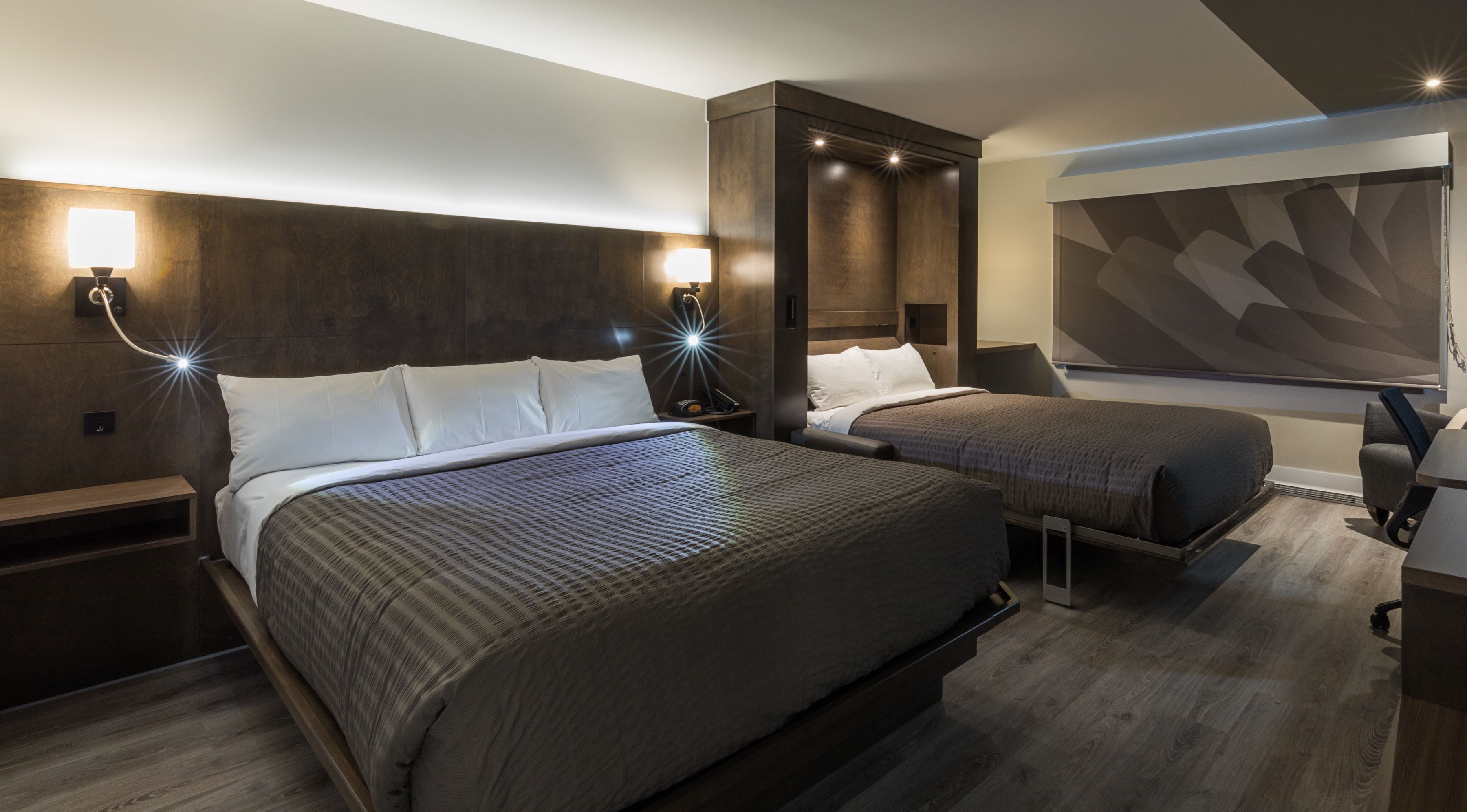 A modern hotel room with two beds, a desk, and a large abstract wall mural.