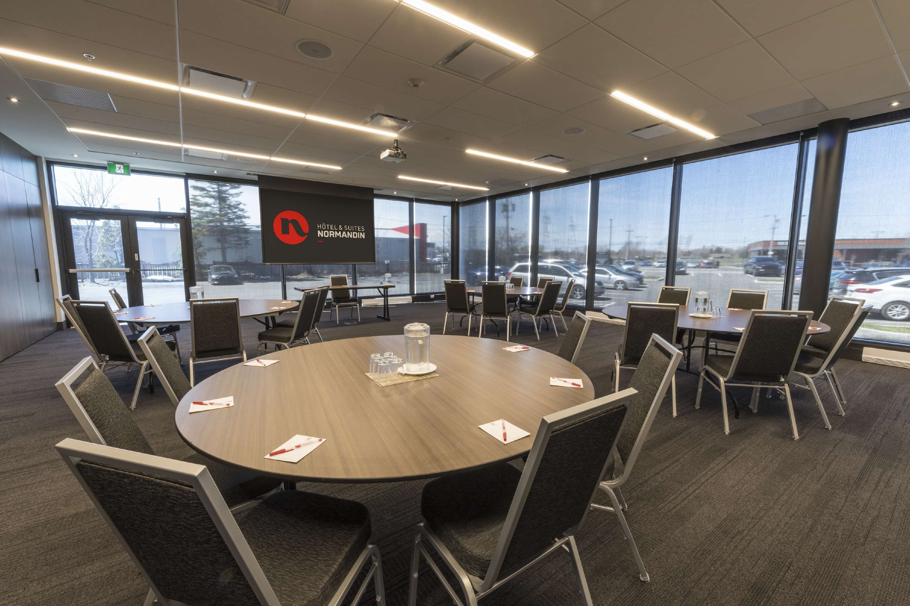 A conference room with a large round table, multiple chairs, and a projector screen displaying the hotel name.