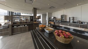 Une cuisine moderne dotée d’un plan de travail en marbre, d’un panier de fruits et d’un espace buffet où sont présentés divers aliments.