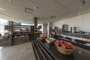A modern kitchen with a marble countertop, a fruit bowl, and a buffet area with various food items.