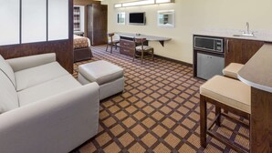 Een compacte hotelkamer met een bank, een kleine eettafel met stoelen, een kitchenette en een aan de muur bevestigde televisie.