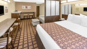 Een hotelkamer met een groot bed, een bureau met stoel, een kitchenette en een badkamer.