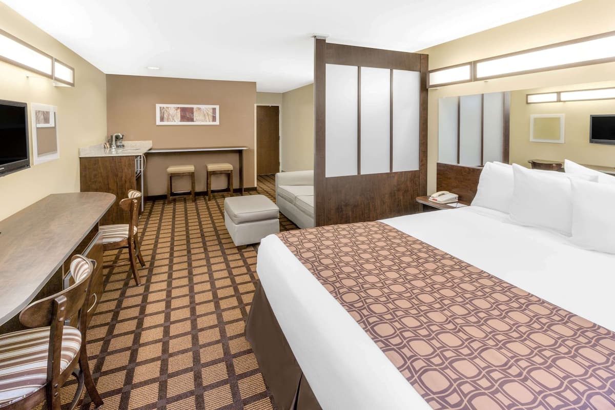 A hotel room with a large bed, a desk with a chair, a small kitchenette, and a bathroom.