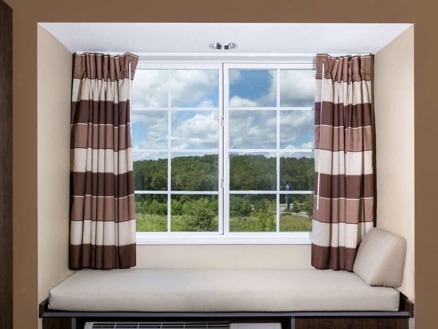 Una habitación con ventana, cortinas, un banco y vistas al verdor.