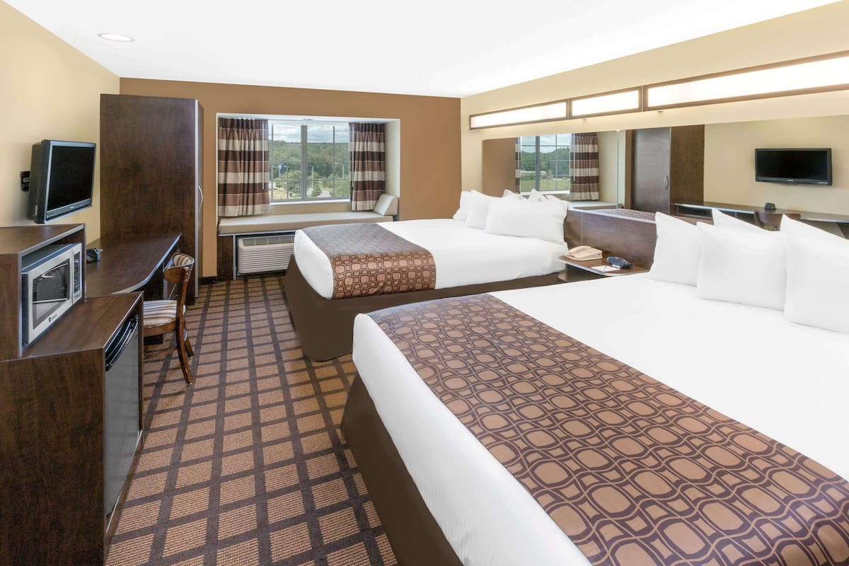 A hotel room with two beds, a desk with a television, a window with curtains, and a view of the outdoors.