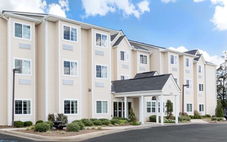 A multi-story hotel with a symmetrical facade, a covered entrance, and a landscaped front yard with a fountain.