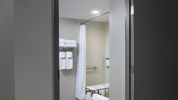 Un baño estrecho con cortina de ducha, un perchero con toallas dobladas y un pequeño banco.