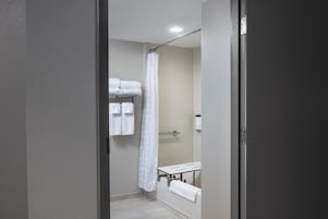 Un baño estrecho con cortina de ducha, un perchero con toallas dobladas y un pequeño banco.