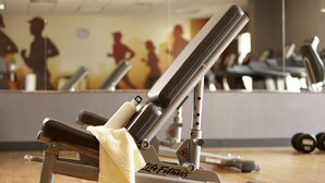Un gimnasio con equipamiento de ejercicio, incluyendo una banca y pesas, y un espejo que refleja siluetas de personas haciendo ejercicio.