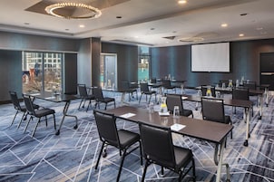 A conference room with multiple tables and chairs, a projector screen, and a large window with a view of buildings.
