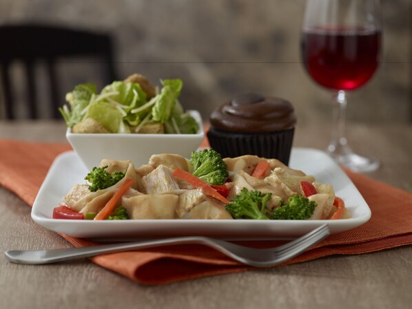 A plate of chicken with vegetables and a cupcake on a table with a wine glass in the background. - HYATT house Charlotte/Center City (Charlotte)
