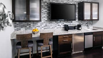 Una cocina moderna con un televisor de pantalla plana grande, armarios oscuros, encimera de granito y dos taburetes de bar.