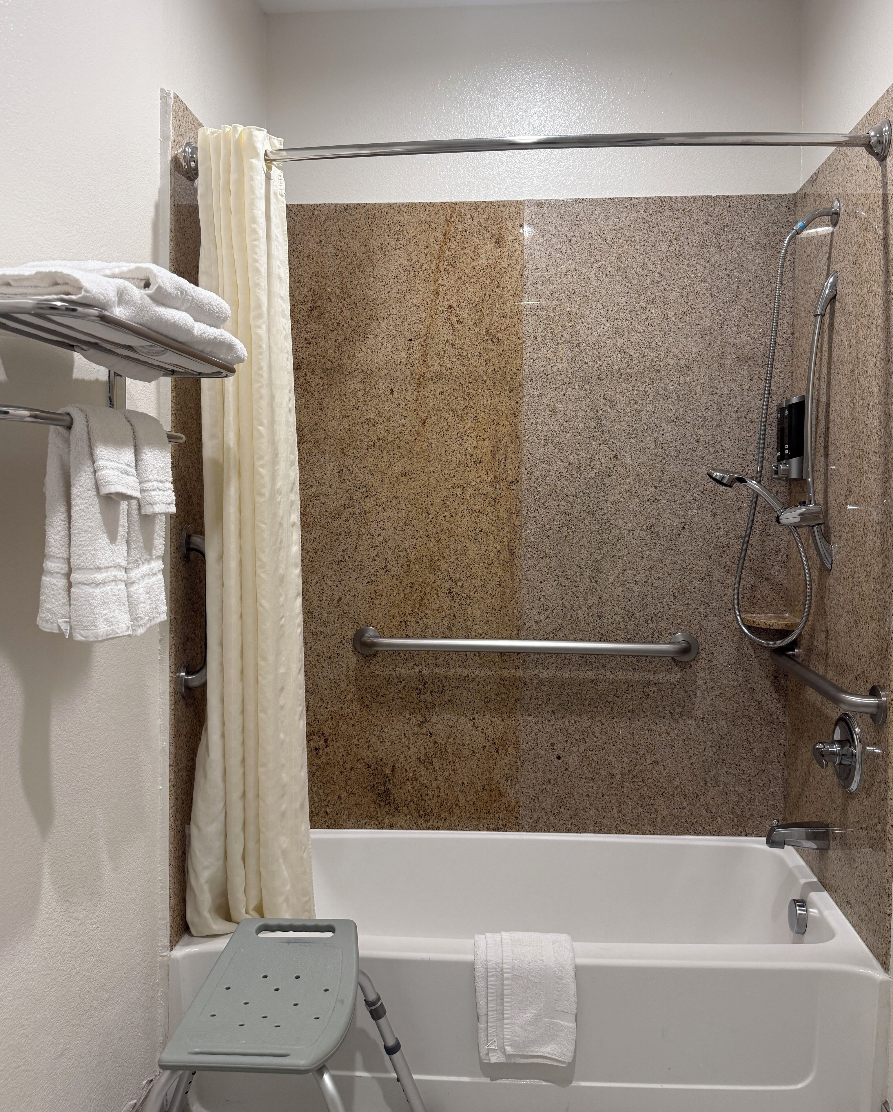 A modern bathroom with a shower, a grab bar, a towel rack, and a handheld showerhead.